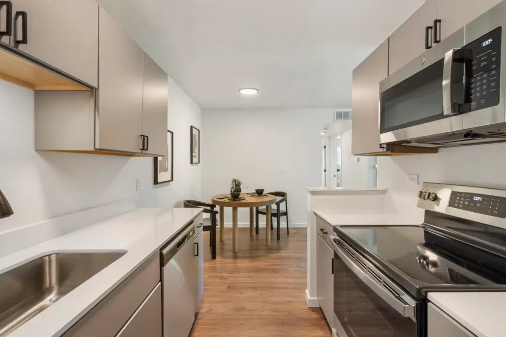 Modern Vineyards on Garland kitchen with gray cabinets, white countertops, stainless steel appliances, wood-style flooring, and dining area in the background.
